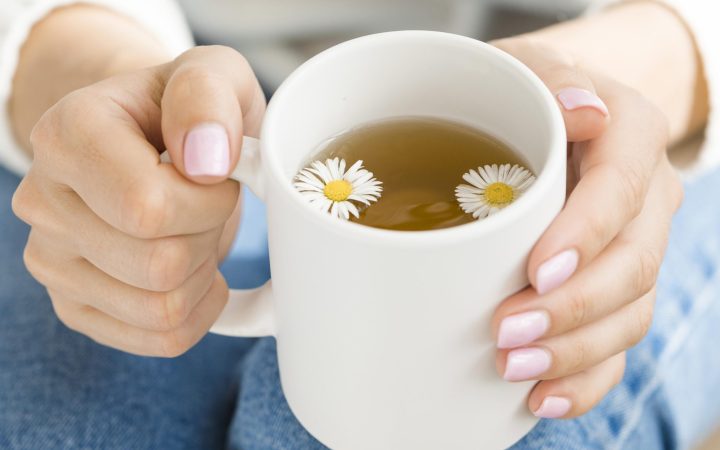 high-angle-woman-holding-white-mug-with-tea-flowers